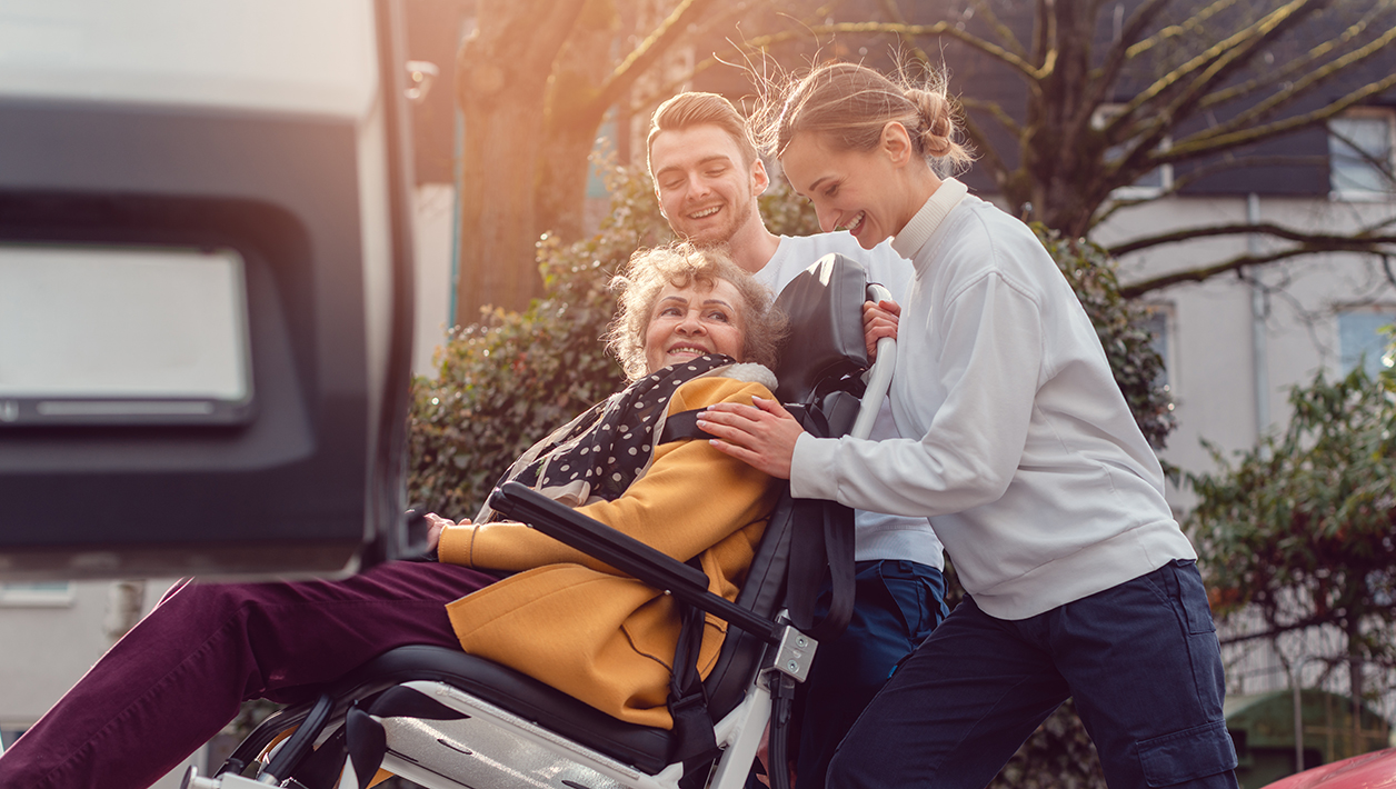 Two helpers picking up disabled senior woman for transport